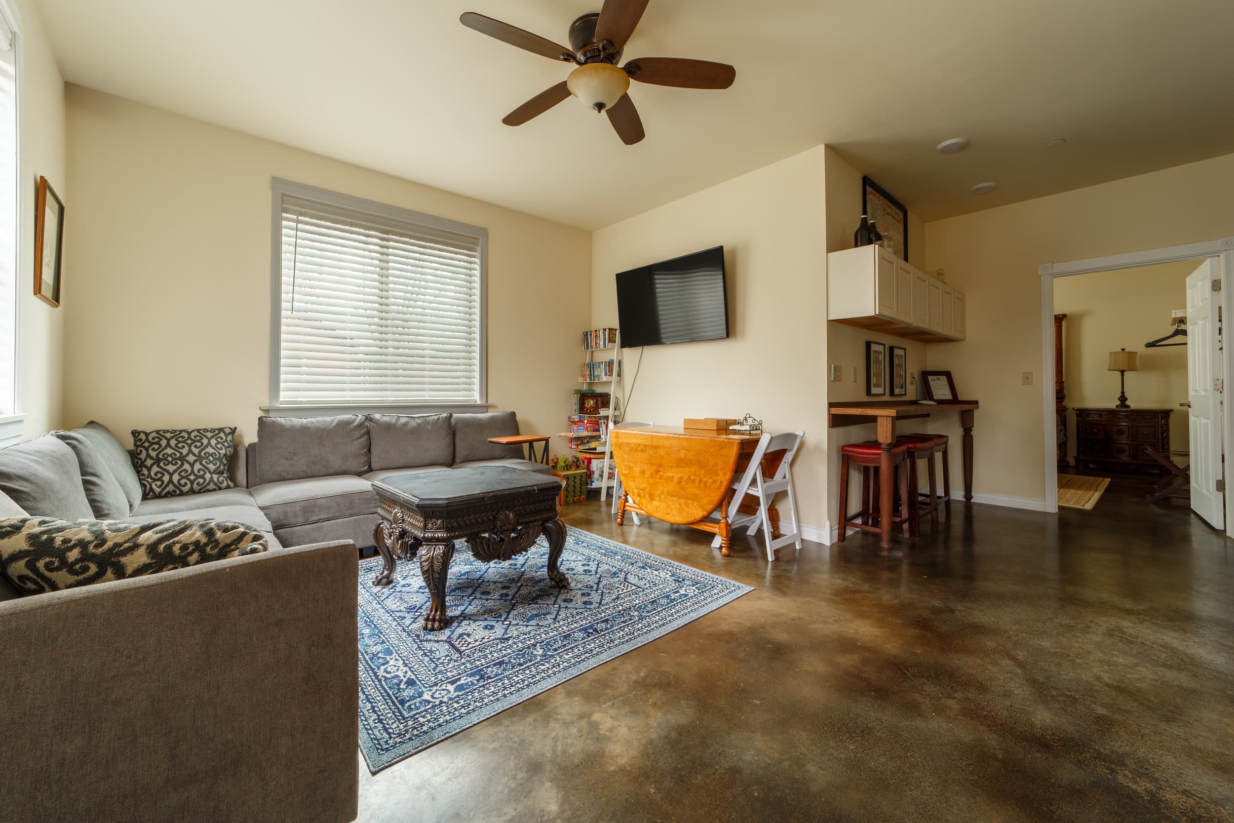 A spacious living area featuring a large, L-shaped gray sectional sofa, a wooden coffee table, and a bright red area rug with a white geometric pattern.