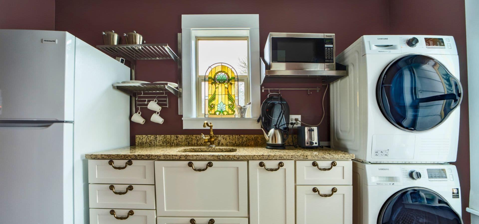 A modern laundry room featuring a refrigerator, microwave, and washer-dryer set against a maroon wall.