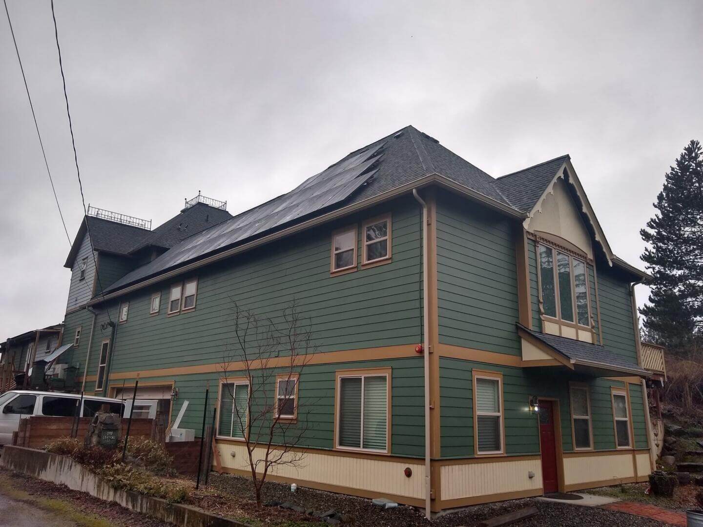 A large green house with multiple levels and a steep roof, surrounded by overcast skies.