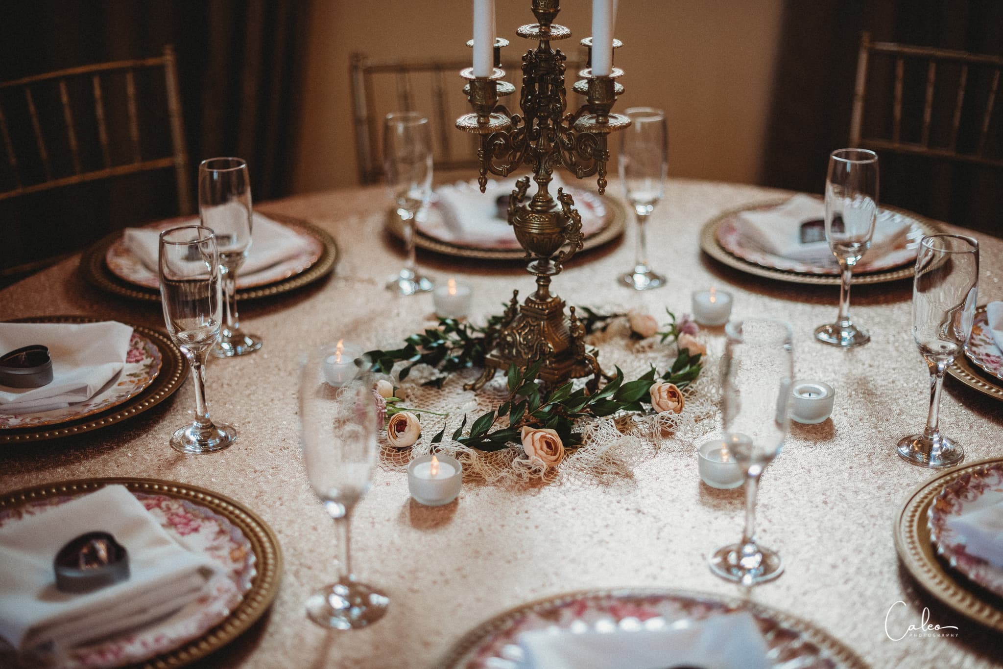Elegant dining table set with plates, glasses, and a centerpiece featuring a candelabrum and flowers.