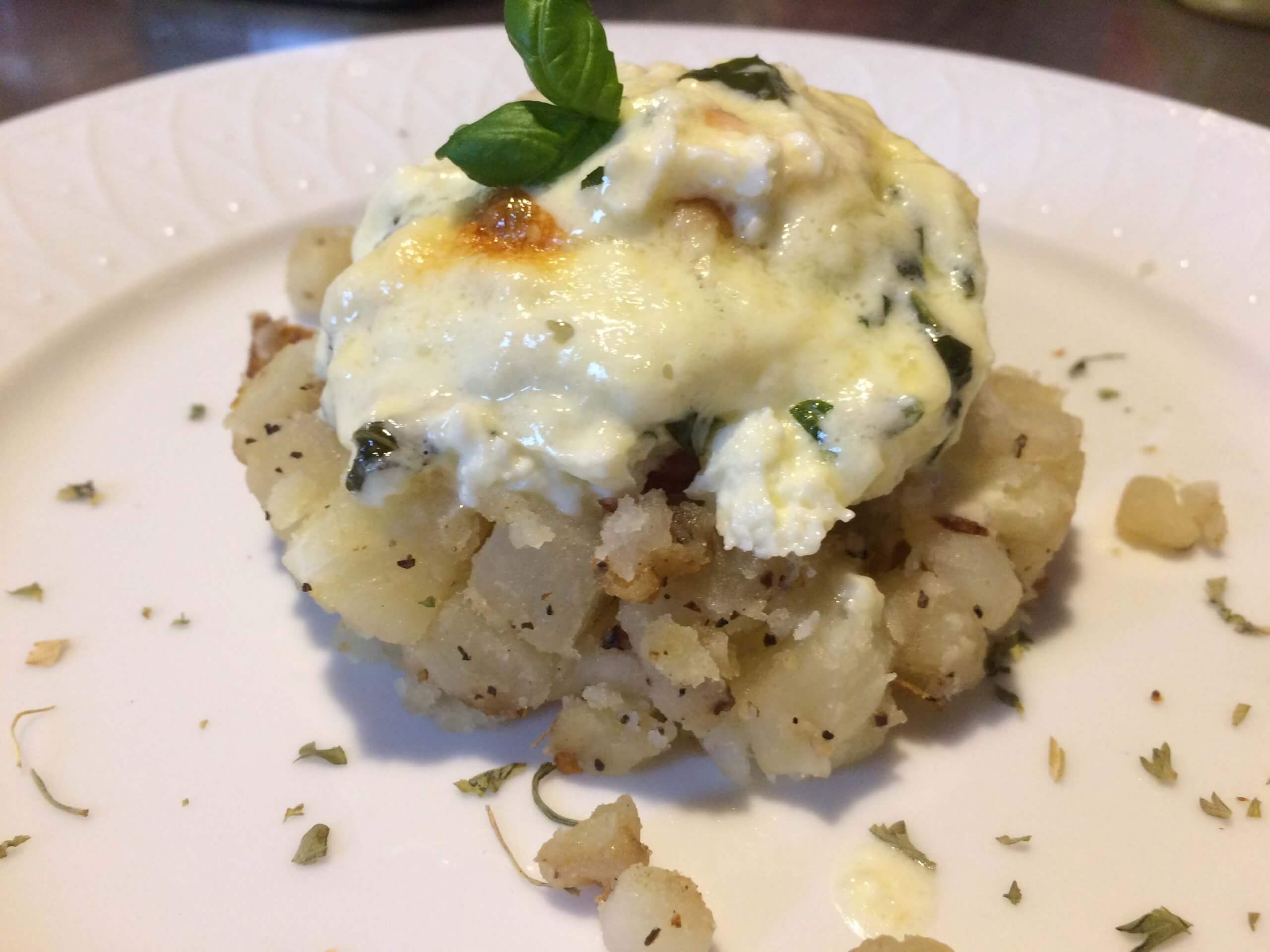 A creamy spinach and cheese topping sits atop a mound of seasoned mashed potatoes, garnished with a basil leaf.