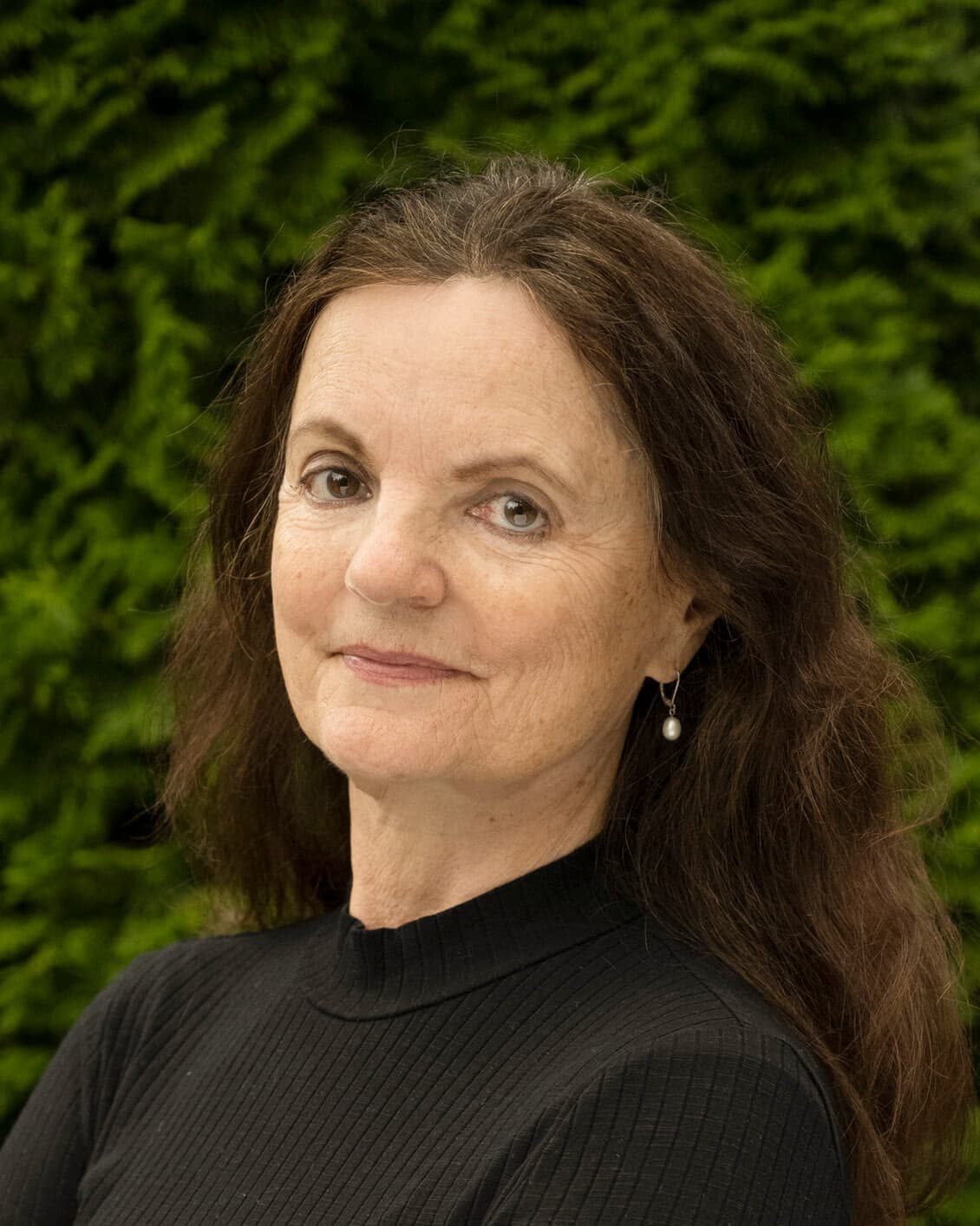A woman with long brown hair and a black turtleneck sweater poses in front of a green backdrop.