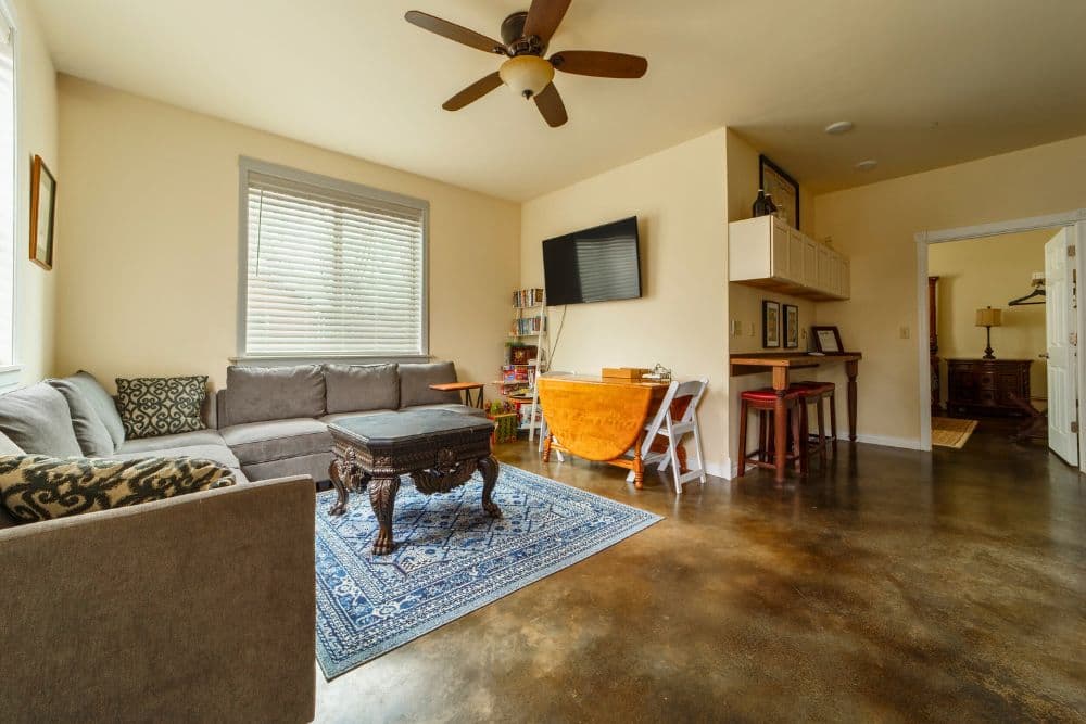 A cozy living room featuring a grey sectional sofa, decorative rug, wooden coffee table, and a flat-screen TV.