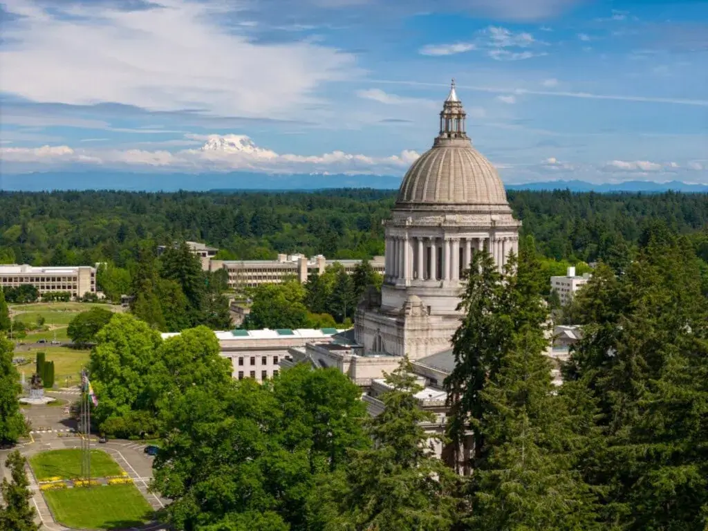 Aerial view of a historic building with a dome, surrounded by green trees and mountains in the background.