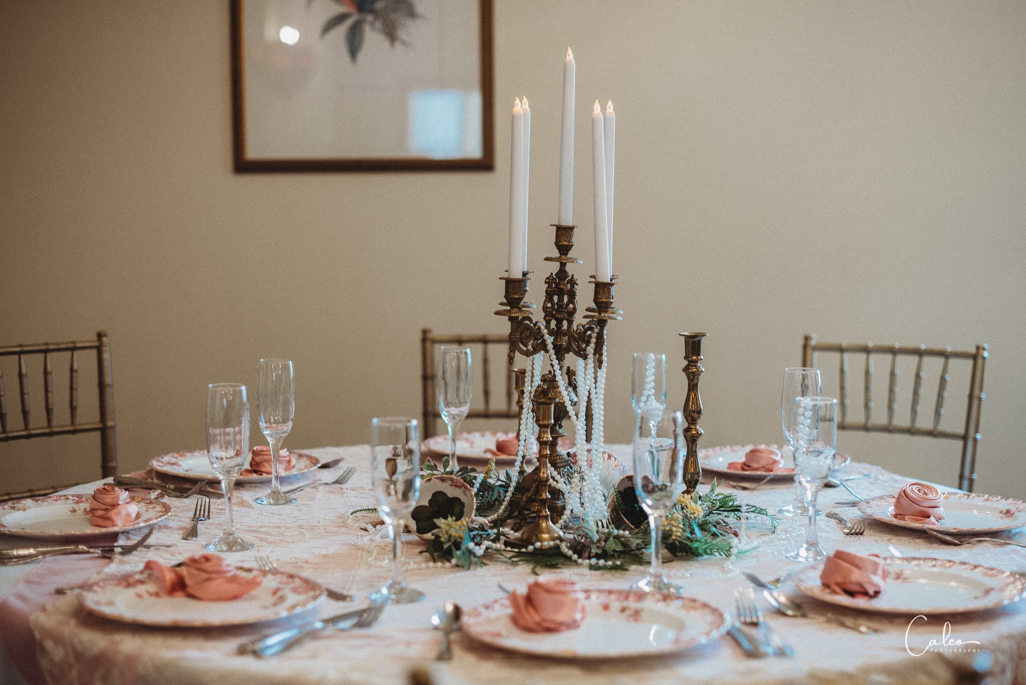 A elegantly set dining table with pink napkins, glassware, and a decorative candle holder centerpiece.