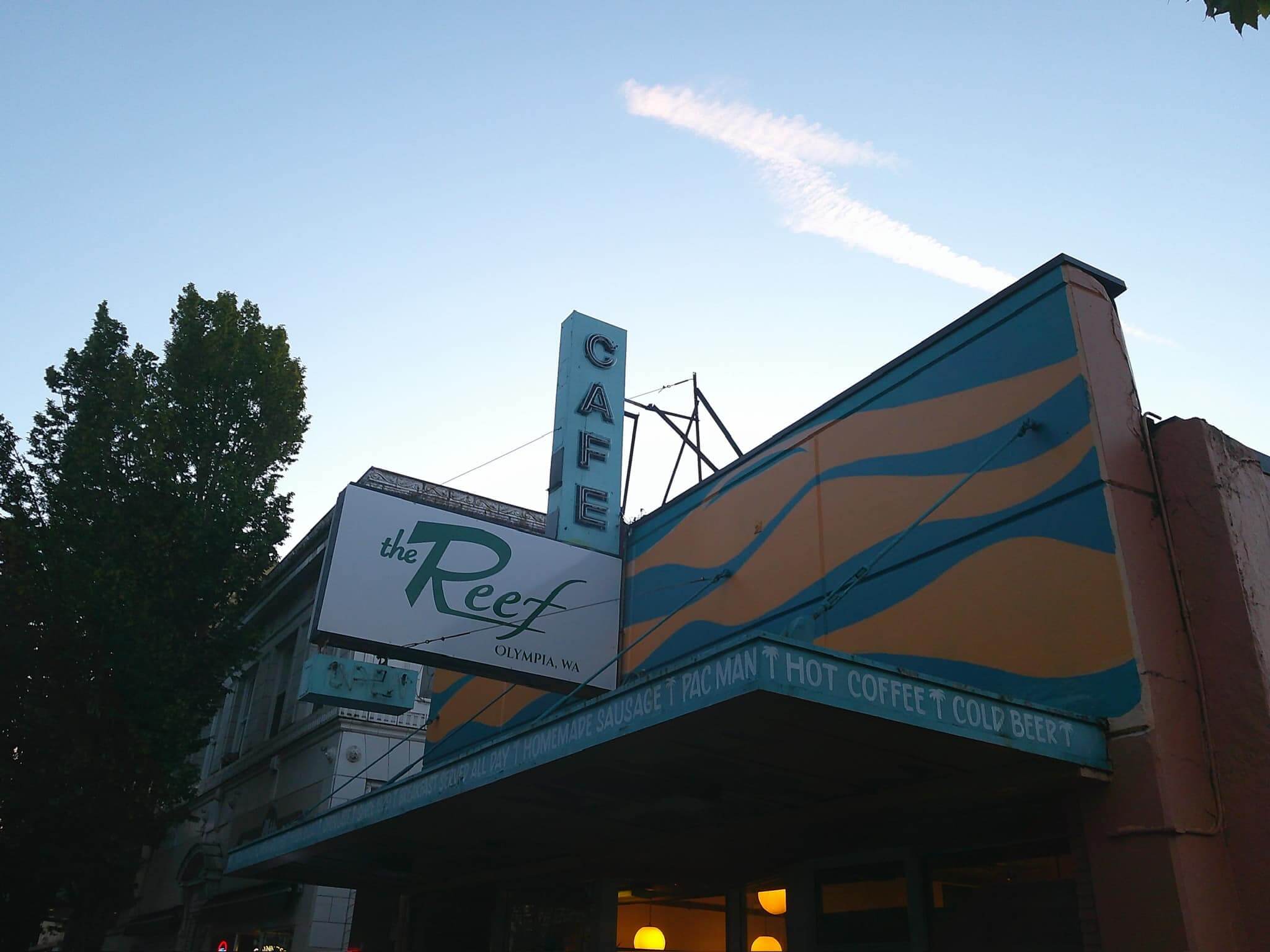 Sign for "The Reef Café" in Olympia, WA, with a colorful retro design against a dusky sky.