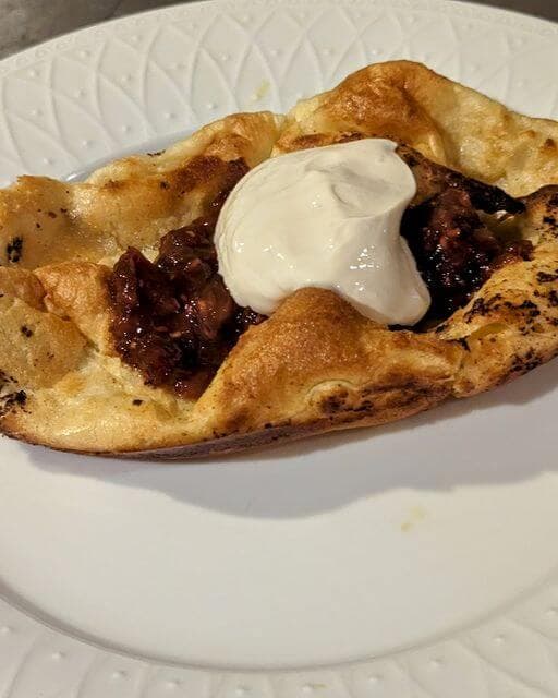 A fluffy, baked bread filled with savory meat and topped with a dollop of sour cream.