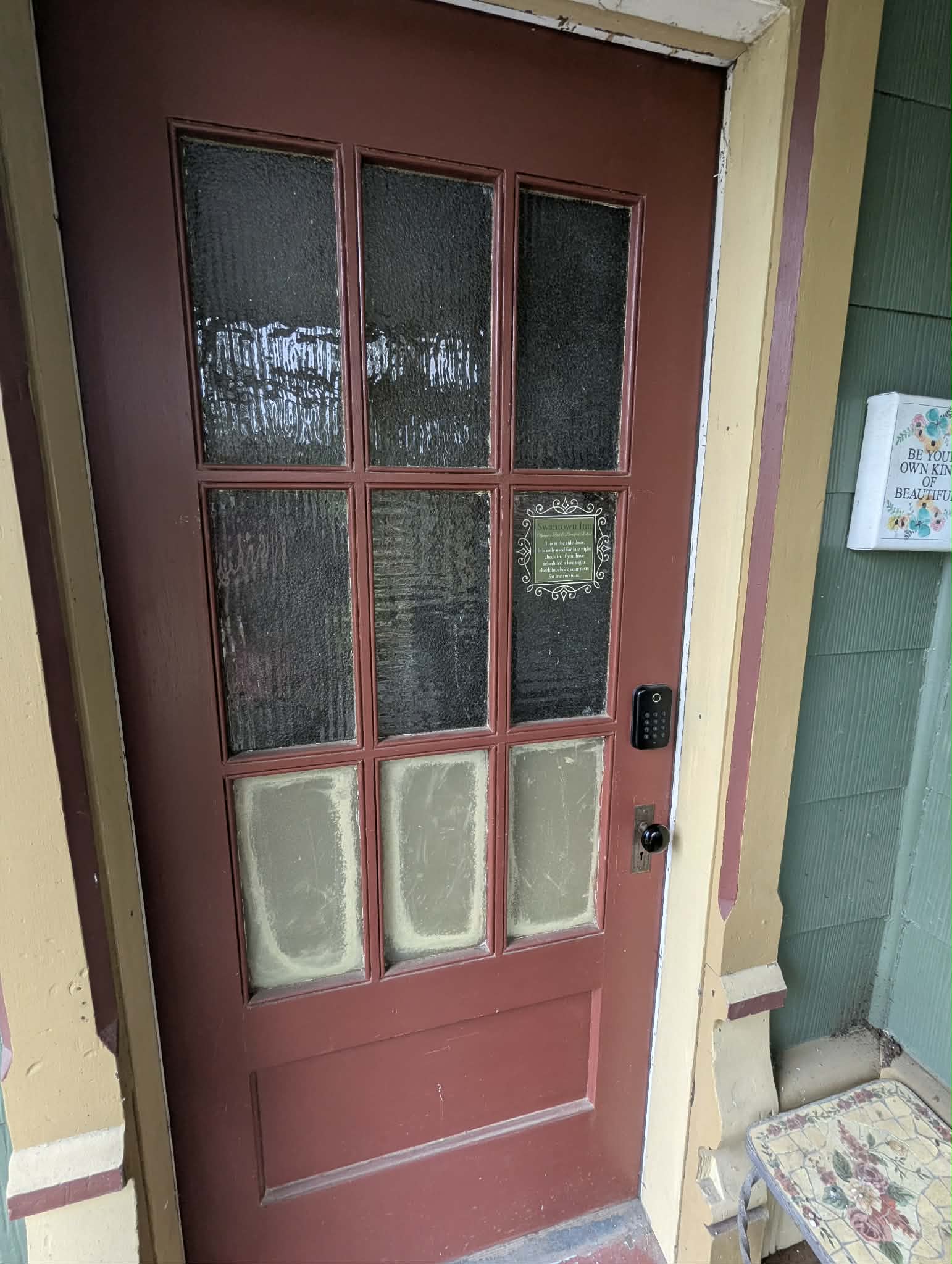 A red door with glass panels on top and a keypad lock, framed by beige and green siding.