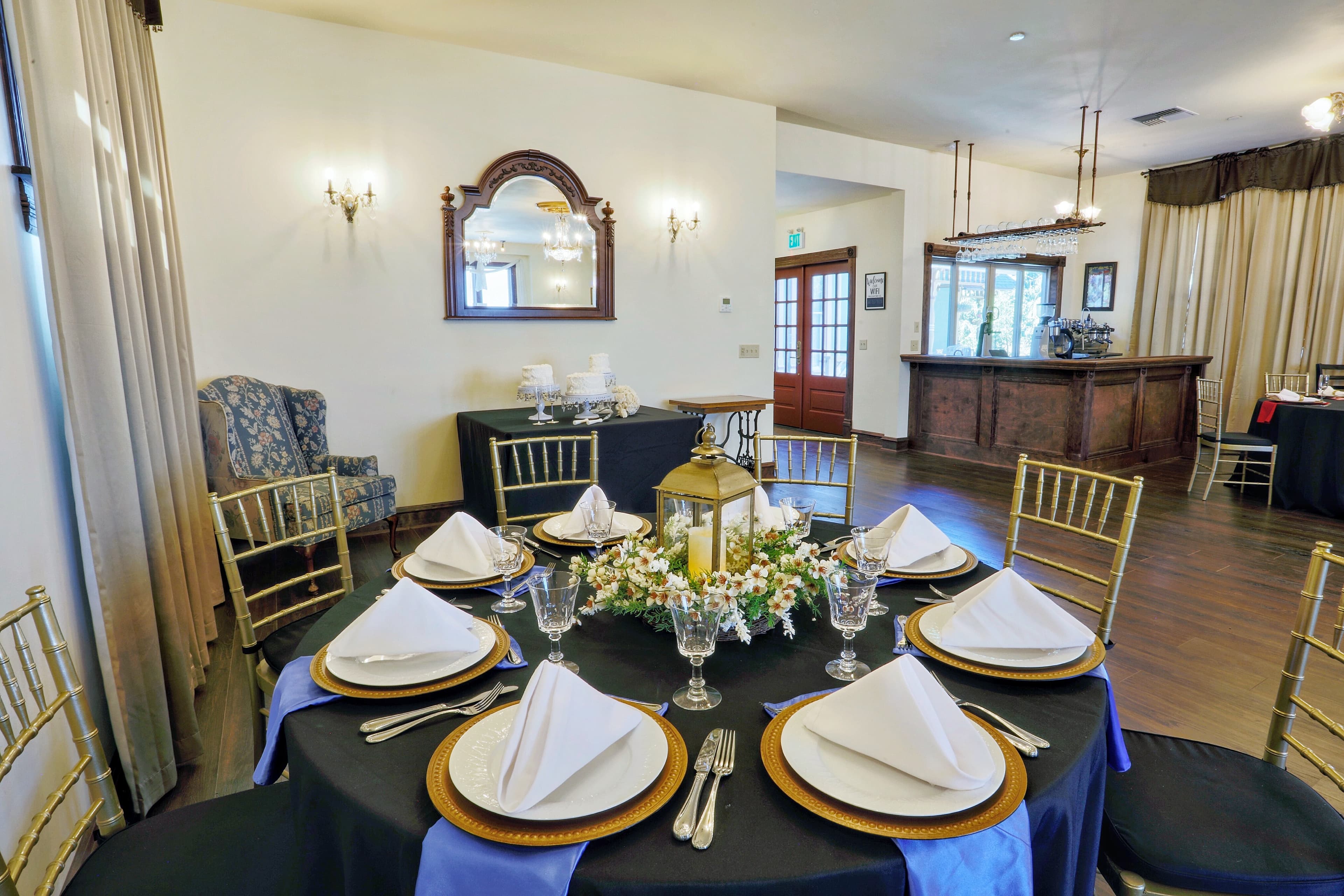 A elegantly set dining table with gold chairs and a floral centerpiece in a well-lit event space.