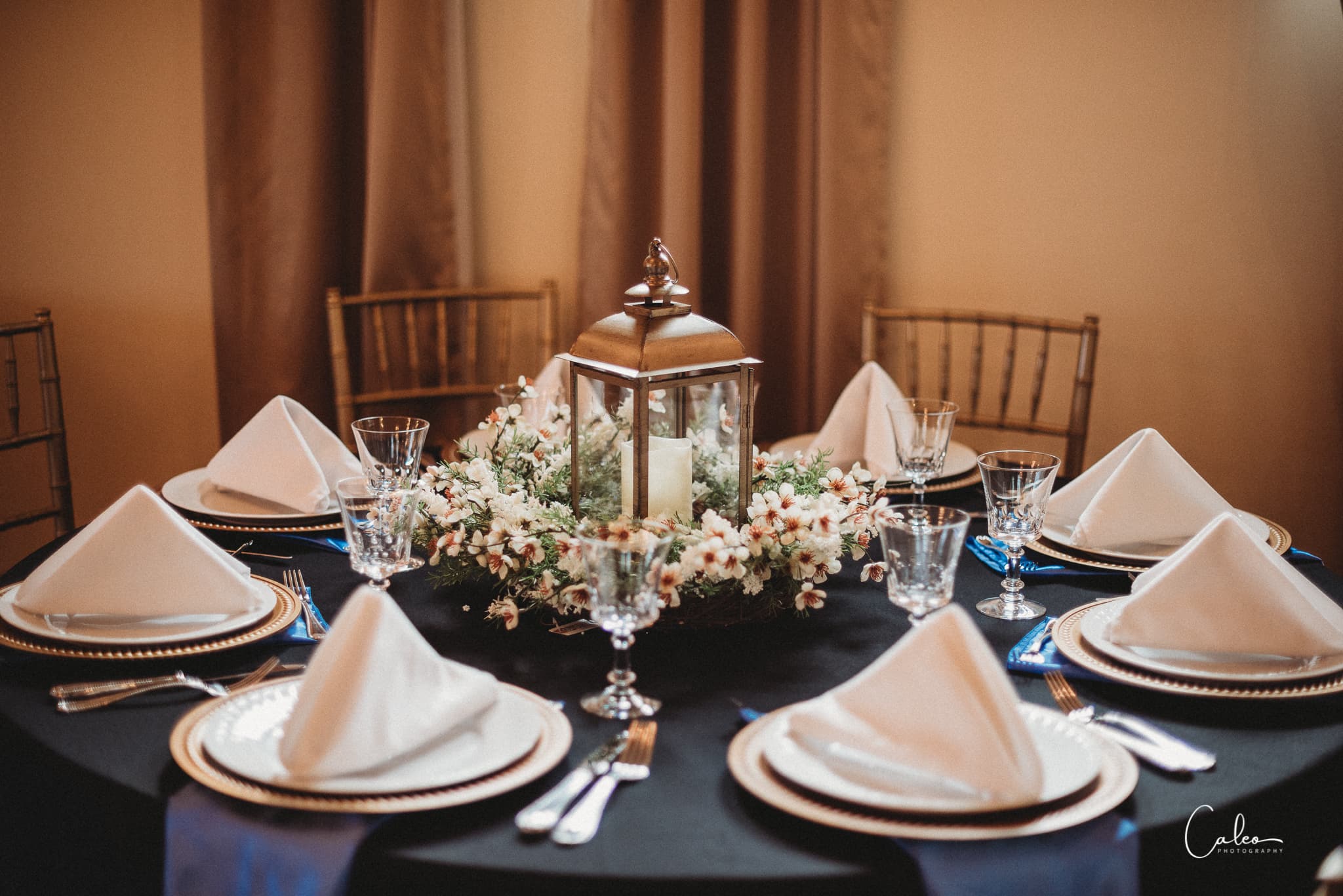 A beautifully set dining table with a centerpiece lantern surrounded by flowers.