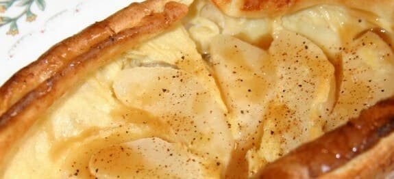 A close-up of a baked dessert topped with sliced apples and a sprinkle of cinnamon.