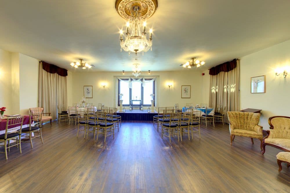 An elegantly furnished ballroom with a chandelier, wooden flooring, and rows of chairs.