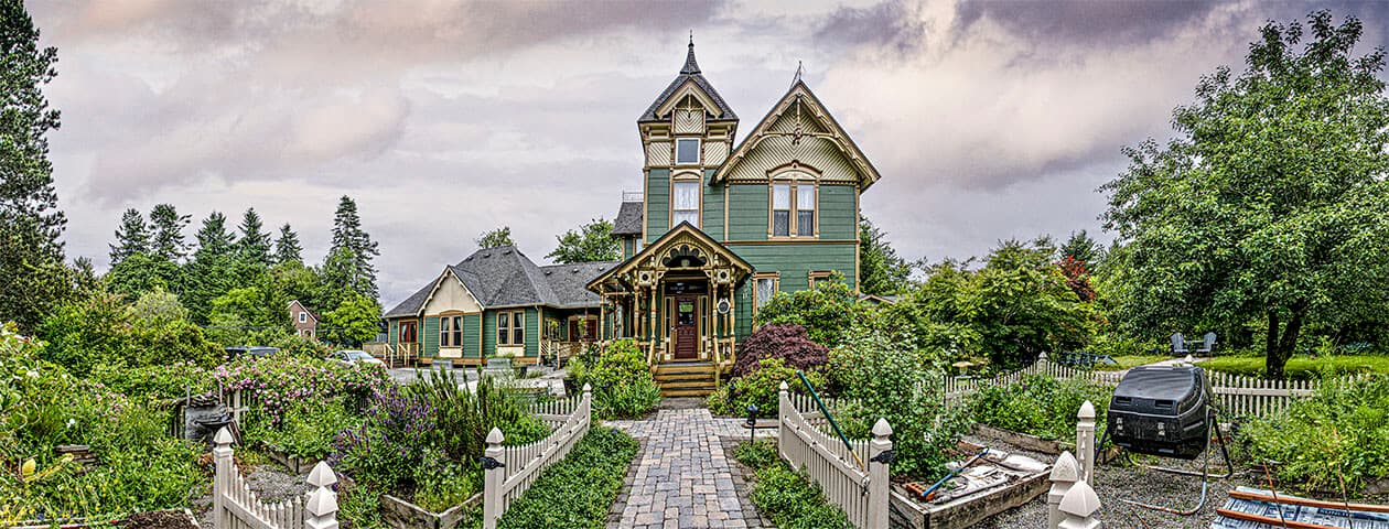 A charming Victorian-style house surrounded by a lush garden and white picket fence.