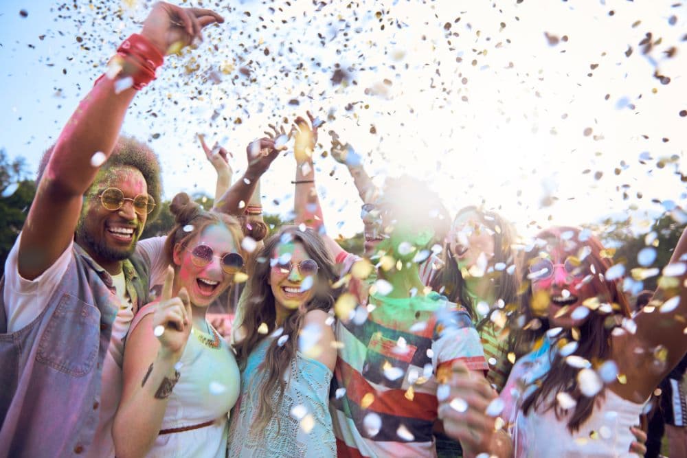 A group of diverse young people celebrate joyfully, surrounded by confetti and sunshine.