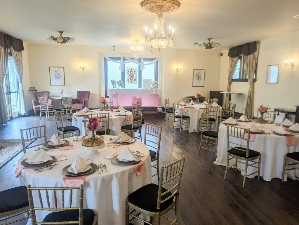 A well-decorated dining room with elegant tables set for a formal event and a chandelier overhead.