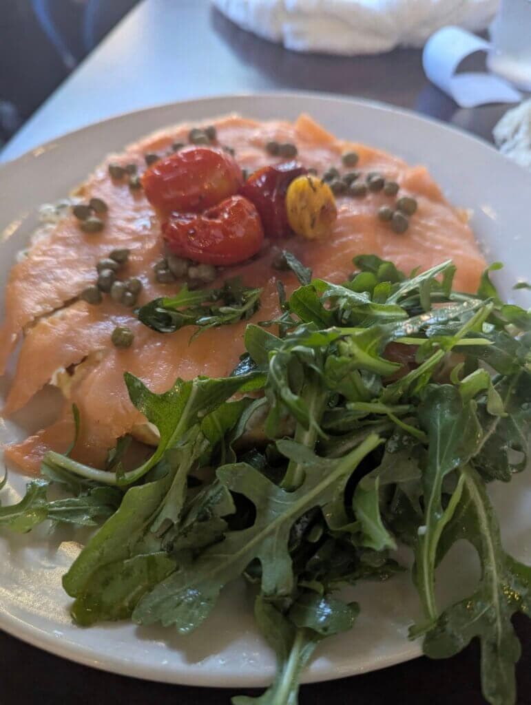 A plate of smoked salmon topped with cherry tomatoes and capers, paired with a side of fresh arugula.