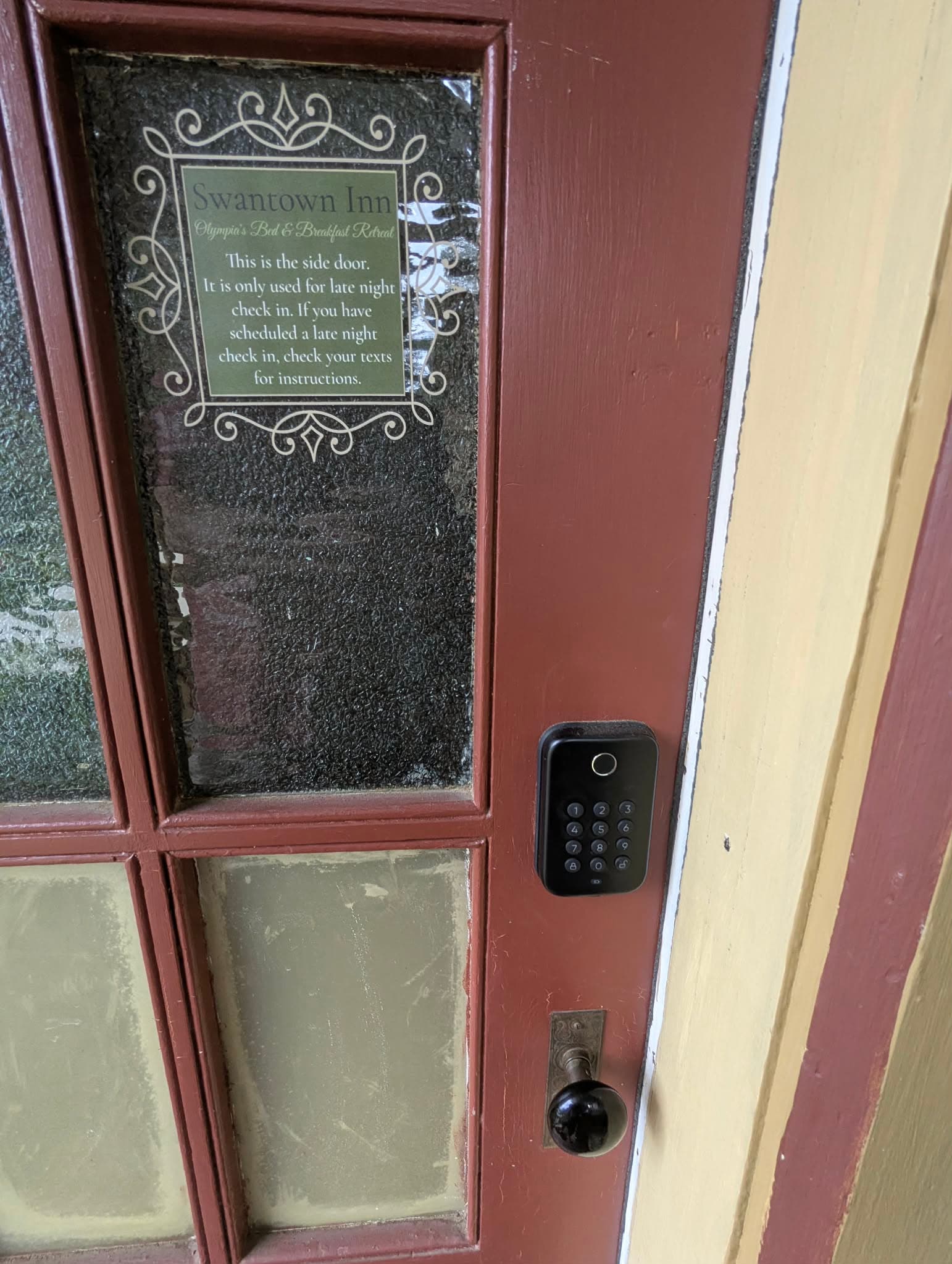 A side door with a keypad lock and a sign for late-night check-in instructions at Swantown Inn.
