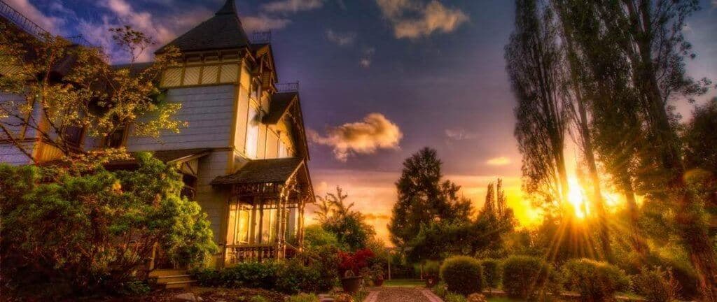 A scenic view of a house illuminated by a sunset, surrounded by lush greenery.