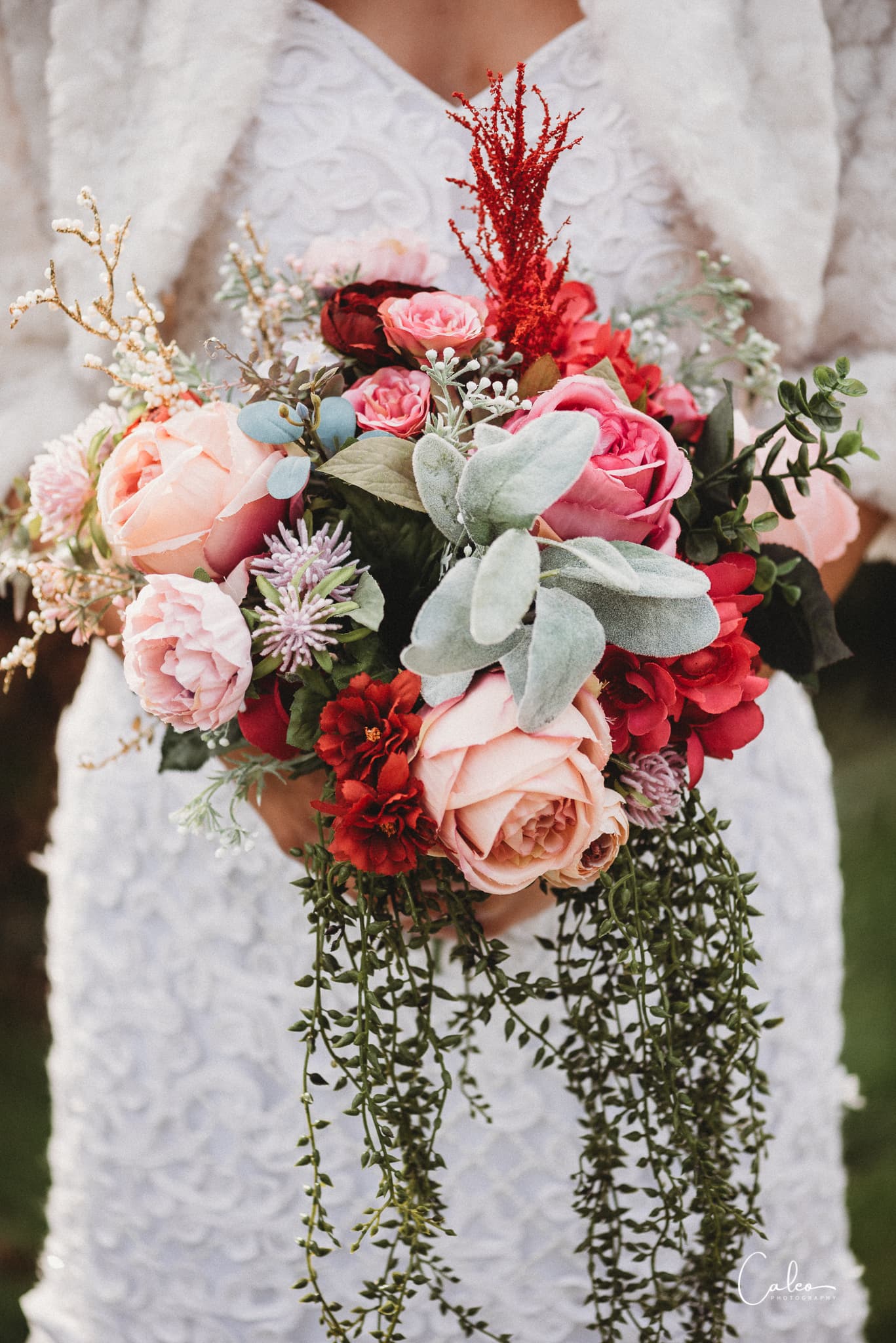 A person holding a vibrant bouquet of assorted flowers in front of a white dress.