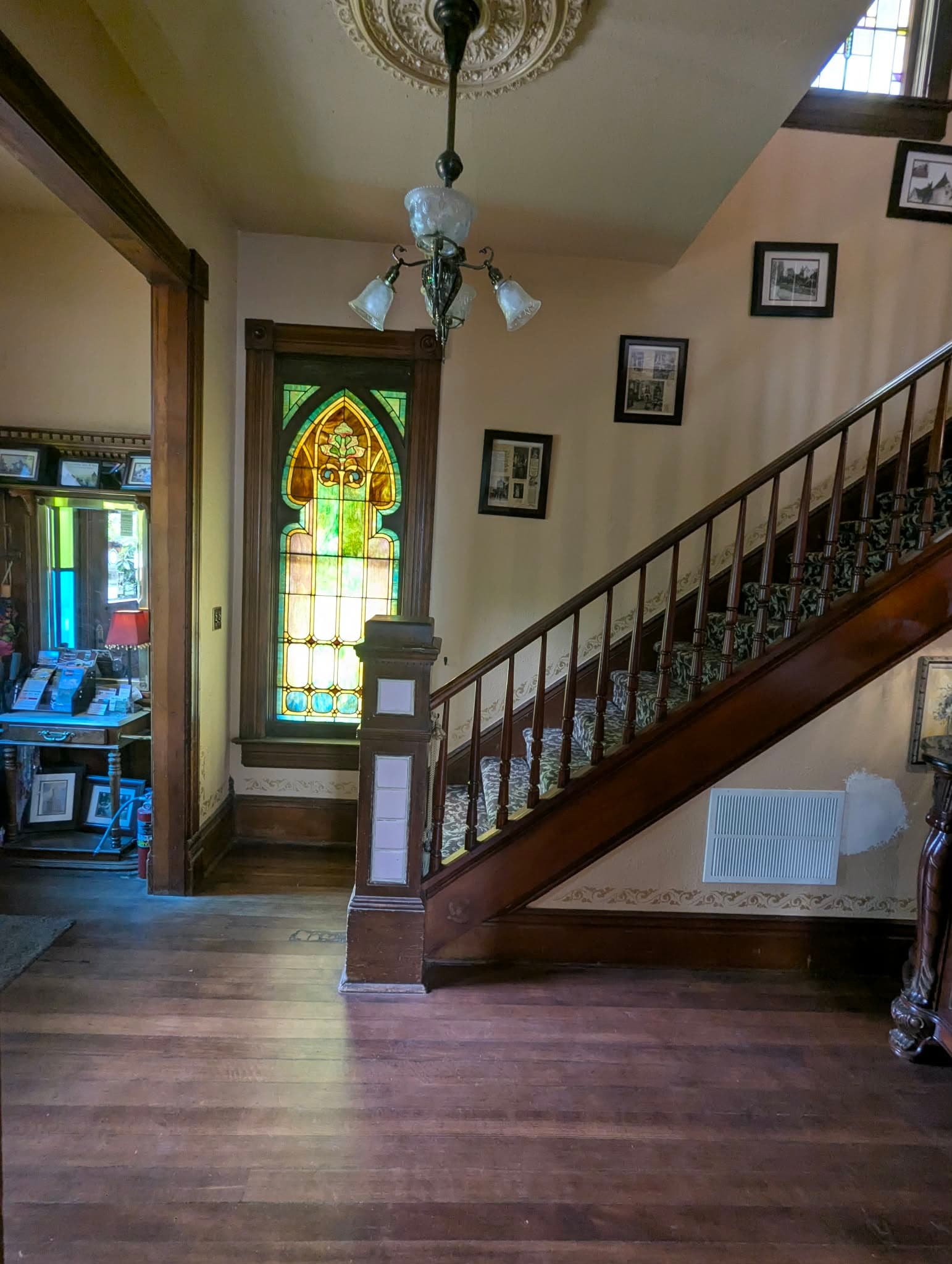A foyer with a wooden staircase and a stained glass window, framed by vintage decor.