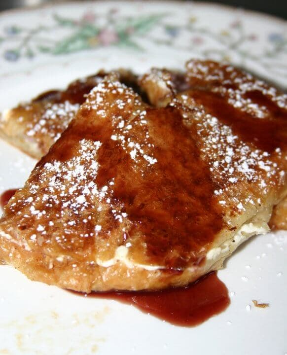 A slice of French toast topped with syrup and powdered sugar on a decorative plate.