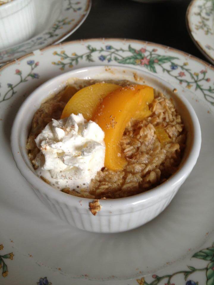 Baked oatmeal topped with peach slices and whipped cream in a white ramekin.