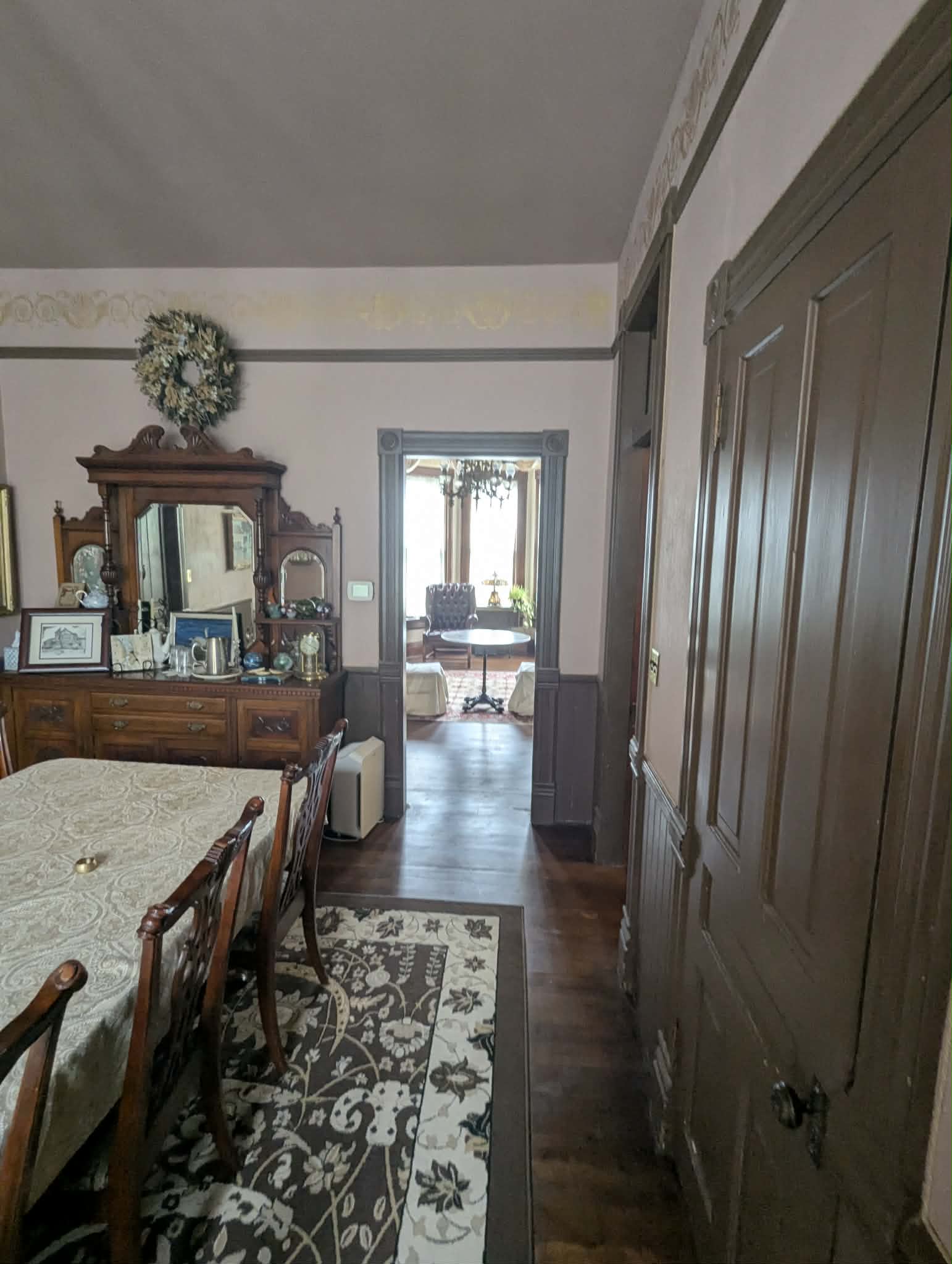 A view of a dining room leading to a sunlit sitting area through an open doorway.