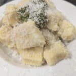 Plate of gnocchi garnished with grated cheese and a sprinkle of herbs.