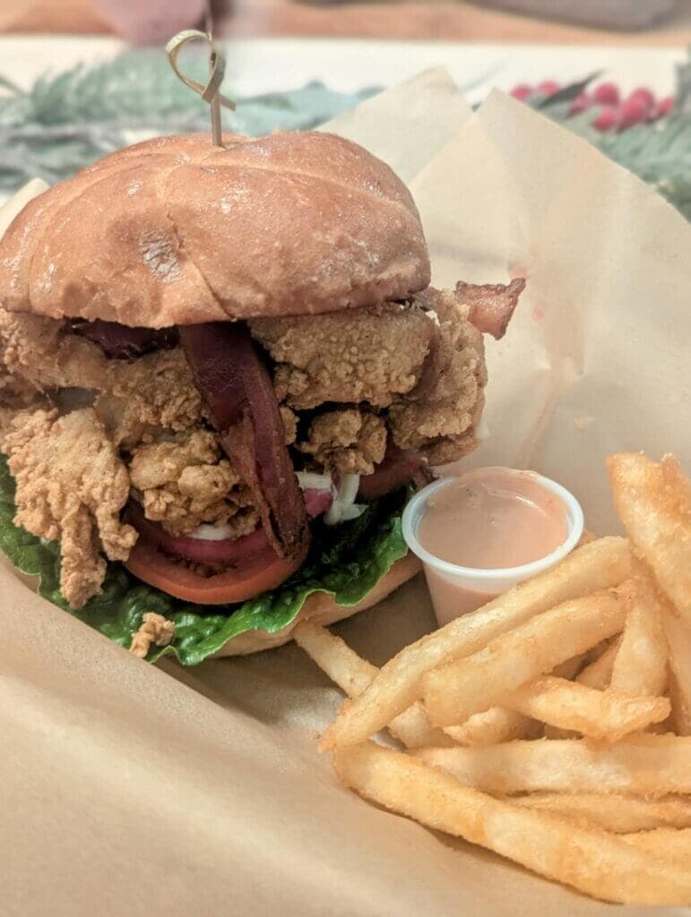 A crispy fried chicken sandwich topped with bacon, lettuce, tomato, and a side of French fries.