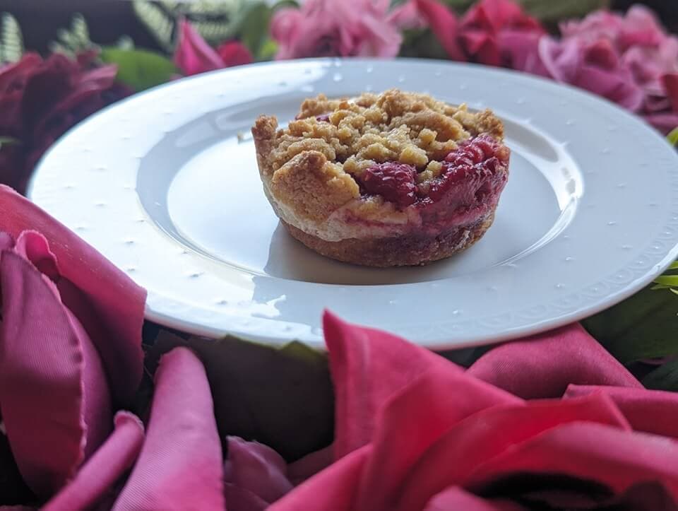 A single berry crumble on a white plate surrounded by pink rose petals.