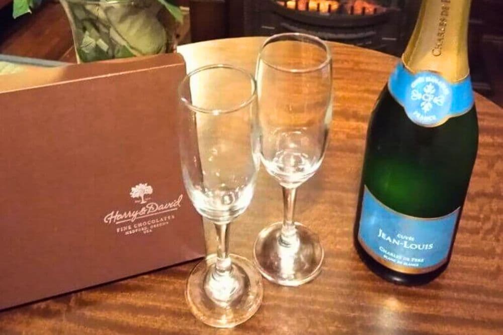 A bottle of sparkling wine beside two empty champagne flutes and a box of chocolates.
